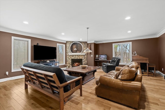 living room featuring recessed lighting, a stone fireplace, light wood-style floors, crown molding, and baseboards