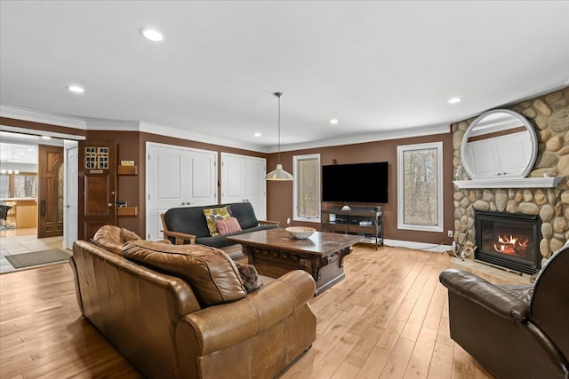 living area with recessed lighting, ornamental molding, a stone fireplace, and light wood-style flooring