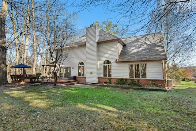 rear view of property with a wooden deck, a shingled roof, brick siding, a yard, and a chimney