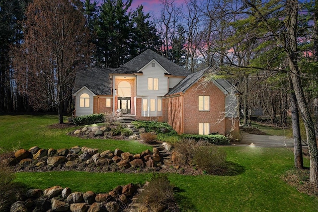 traditional home featuring roof with shingles, brick siding, and a yard