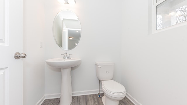 half bathroom with baseboards, wood finished floors, and toilet