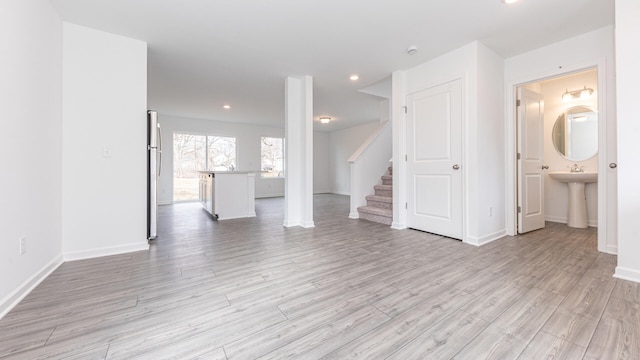 unfurnished living room with light wood-style flooring, baseboards, recessed lighting, and stairs