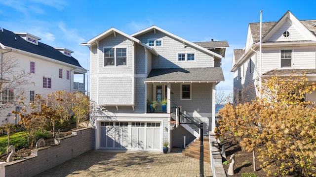 view of front facade with an attached garage, a shingled roof, stairway, and decorative driveway