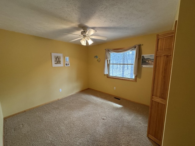 unfurnished bedroom with ceiling fan, a textured ceiling, visible vents, baseboards, and light carpet
