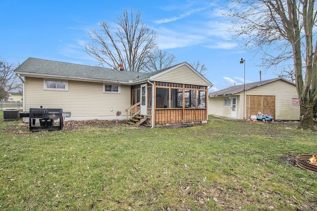 rear view of property featuring cooling unit, a lawn, a fire pit, and a sunroom