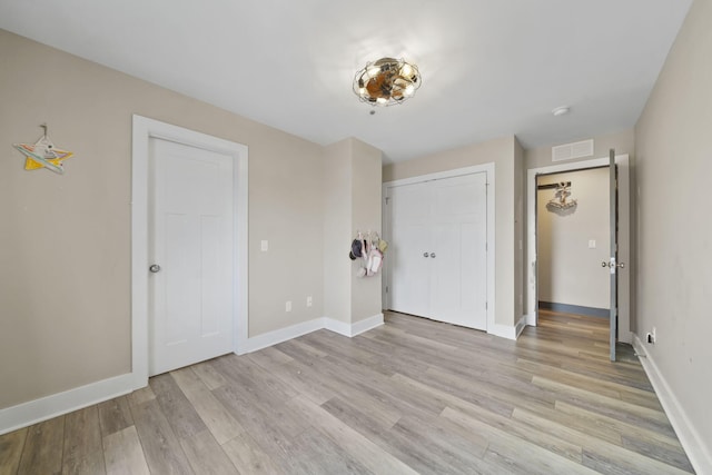 unfurnished bedroom with light wood-type flooring, a closet, baseboards, and visible vents