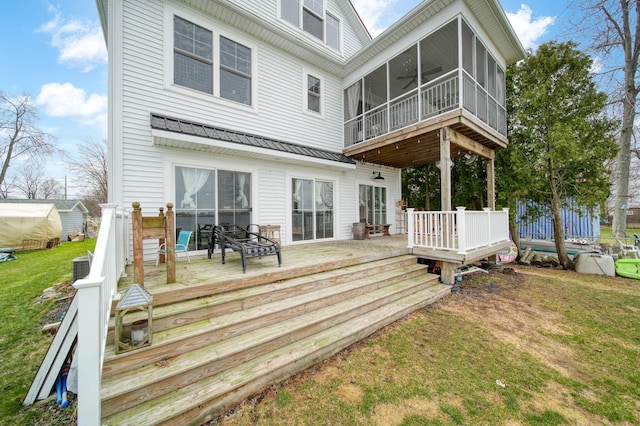 back of property with a sunroom, a wooden deck, and a lawn