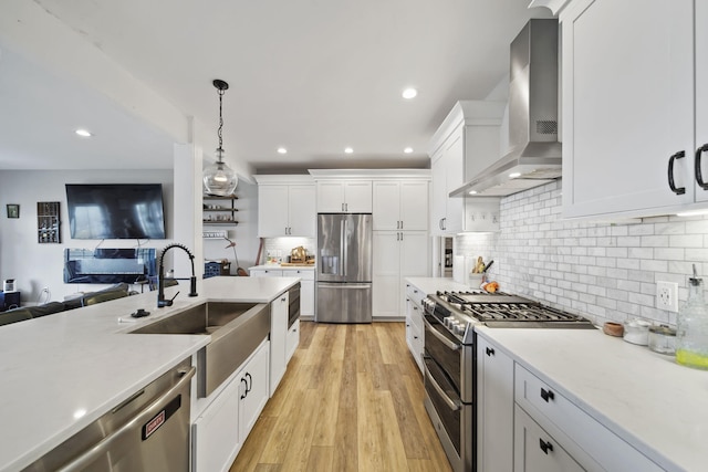 kitchen featuring wall chimney range hood, recessed lighting, a sink, and appliances with stainless steel finishes