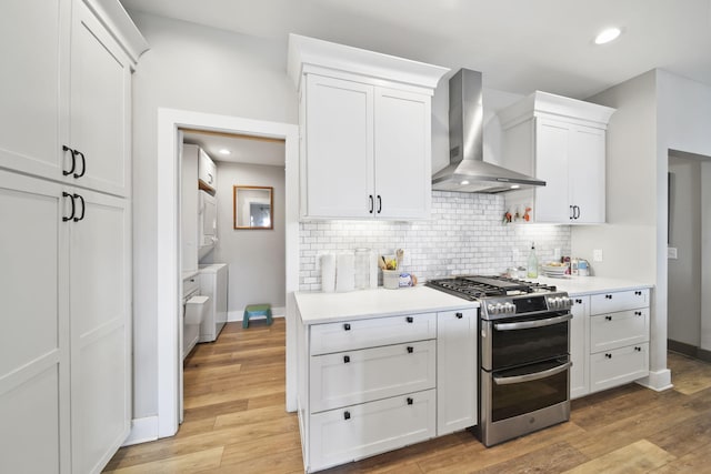 kitchen with white cabinets, wall chimney range hood, light countertops, double oven range, and backsplash