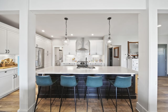 kitchen featuring stainless steel fridge, a sink, wall chimney range hood, a kitchen bar, and backsplash