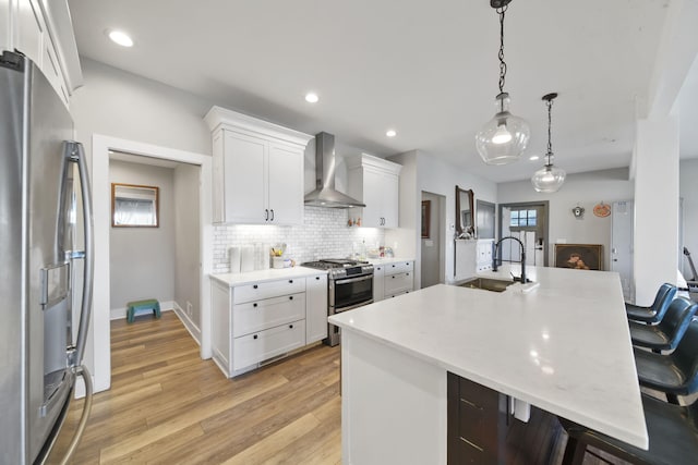 kitchen with wall chimney exhaust hood, a sink, light countertops, appliances with stainless steel finishes, and a breakfast bar area