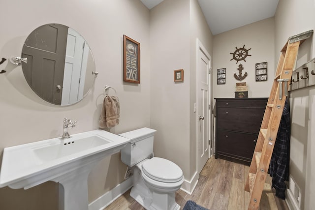 half bath with baseboards, toilet, visible vents, a sink, and wood finished floors