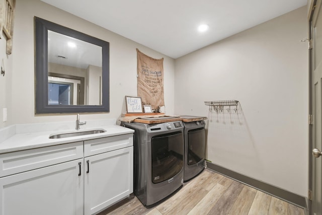laundry area featuring separate washer and dryer, light wood finished floors, a sink, and cabinet space