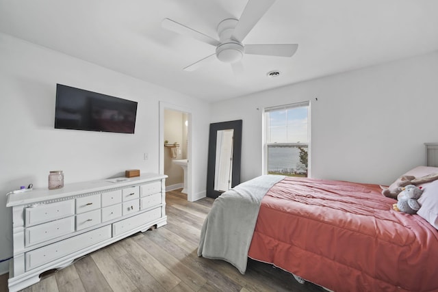 bedroom featuring light wood-style flooring, ensuite bathroom, a ceiling fan, and visible vents