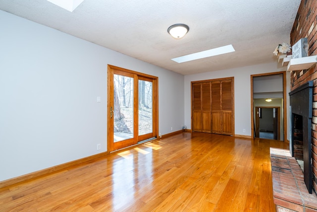 2532 Ridgewood Trl, Berrien Springs, MI 49103 - unfurnished living room with baseboards, light wood-type flooring, a fireplace, a textured ceiling, and a skylight