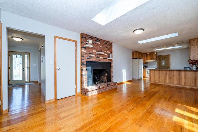 2532 Ridgewood Trl, Berrien Springs, MI 49103 - unfurnished living room featuring a skylight, a brick fireplace, a textured ceiling, and light wood-type flooring
