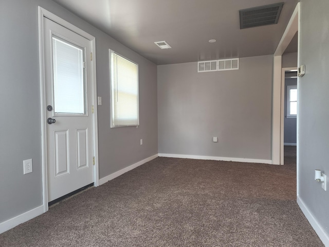 spare room with dark carpet, visible vents, and baseboards