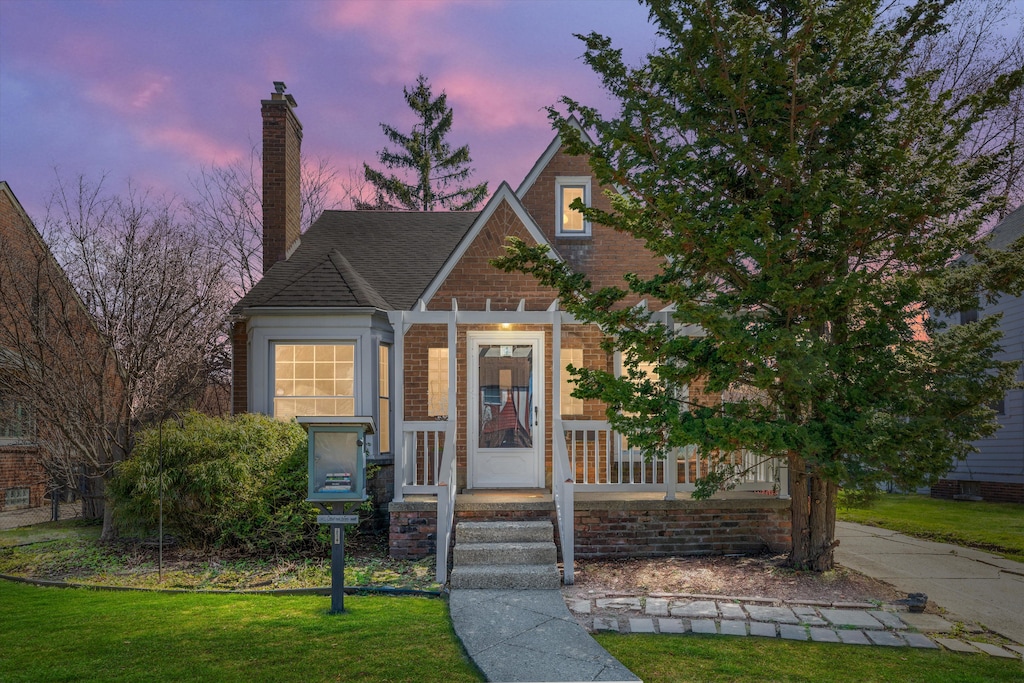 view of front of home with brick siding, a lawn, and a chimney