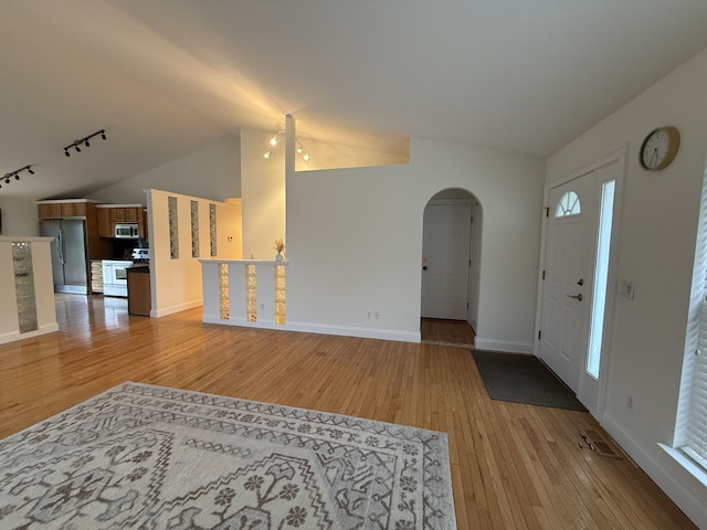 entrance foyer with light wood-style floors, arched walkways, track lighting, and lofted ceiling