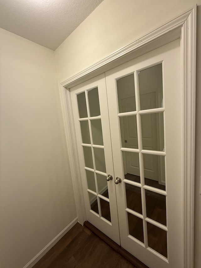 doorway with french doors, a textured ceiling, baseboards, and dark wood-type flooring