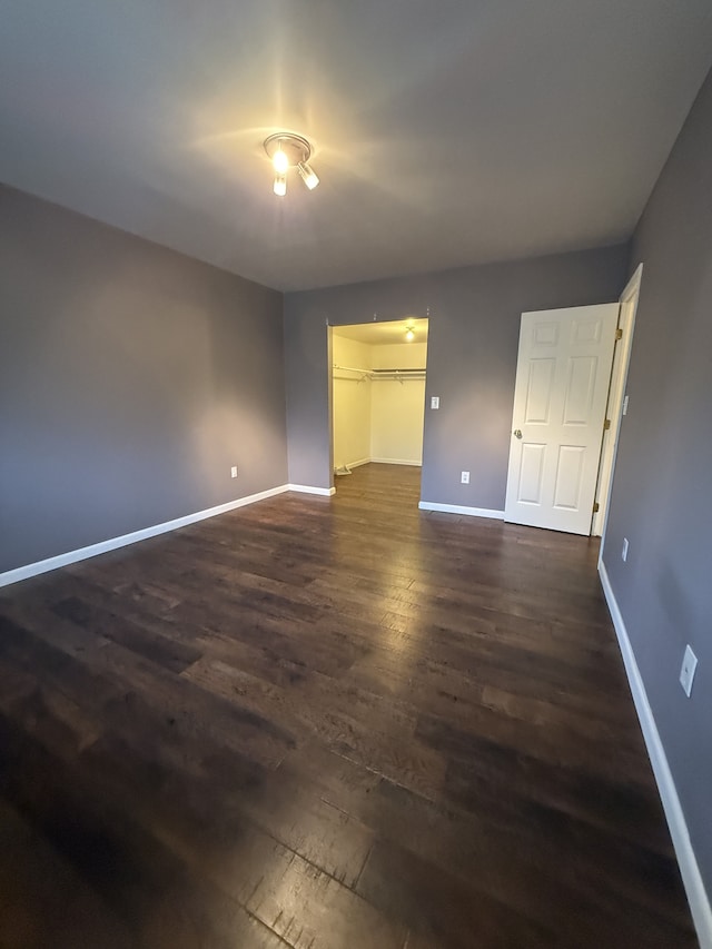 unfurnished bedroom featuring baseboards, a walk in closet, a closet, and dark wood-type flooring