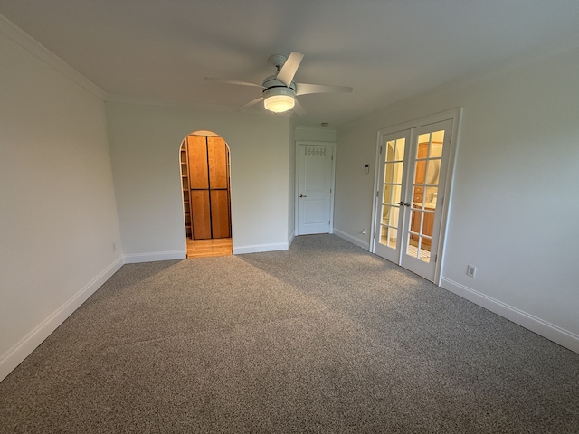 carpeted empty room with french doors, arched walkways, a ceiling fan, and baseboards