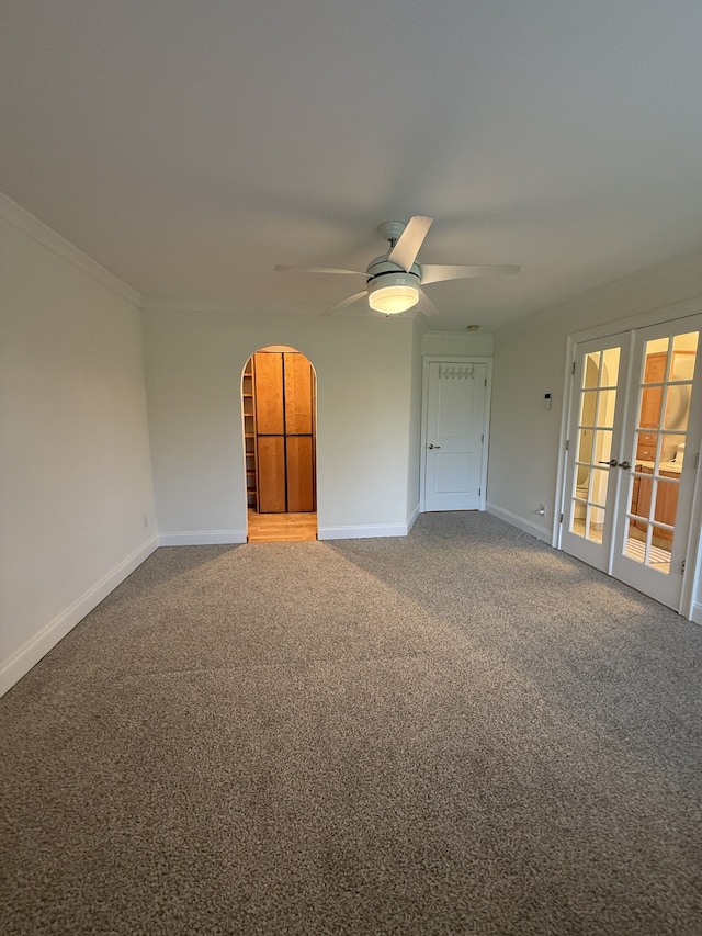 carpeted spare room featuring crown molding, arched walkways, baseboards, and ceiling fan