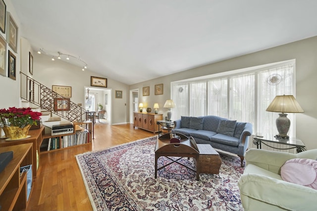 living area featuring wood finished floors, vaulted ceiling, plenty of natural light, and stairs