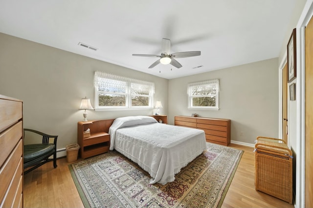 bedroom featuring light wood-type flooring, a baseboard heating unit, ceiling fan, and visible vents
