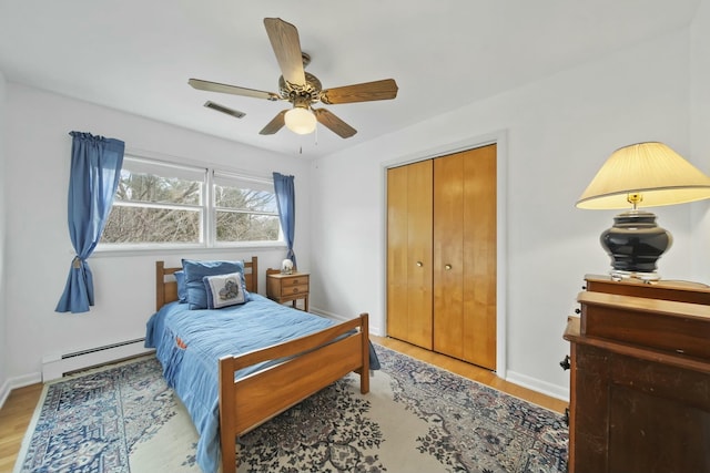 bedroom featuring a closet, a baseboard heating unit, baseboards, visible vents, and wood finished floors