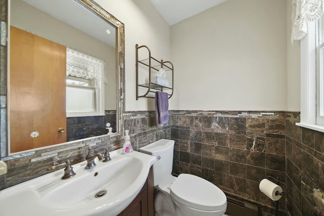 half bath featuring toilet, vanity, a wainscoted wall, and tile walls