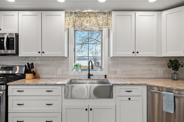 kitchen with a sink, backsplash, white cabinets, and appliances with stainless steel finishes