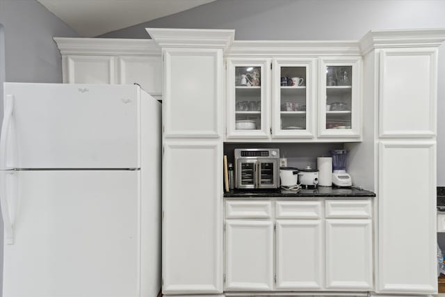 kitchen featuring glass insert cabinets, white cabinets, freestanding refrigerator, and vaulted ceiling
