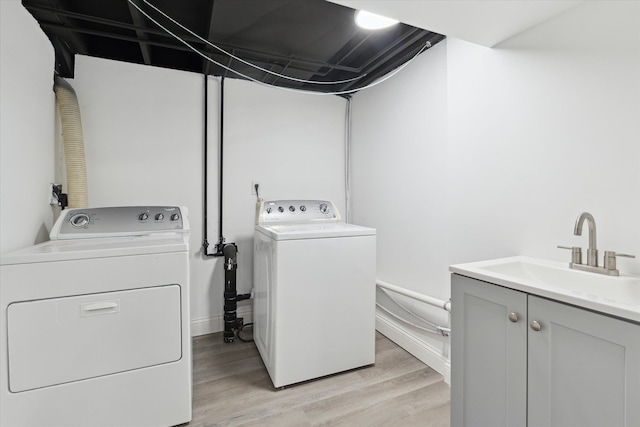 laundry area featuring a sink, cabinet space, separate washer and dryer, and light wood-style floors