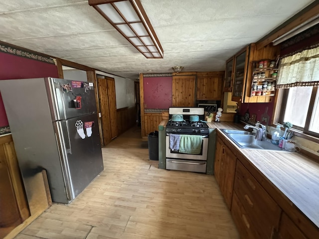 kitchen with glass insert cabinets, a sink, brown cabinetry, stainless steel appliances, and light wood-style flooring