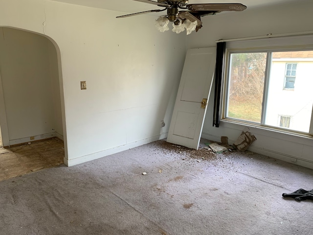 carpeted spare room with baseboards, a ceiling fan, and arched walkways
