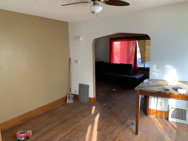 interior space with baseboards, arched walkways, ceiling fan, a textured ceiling, and wood finished floors