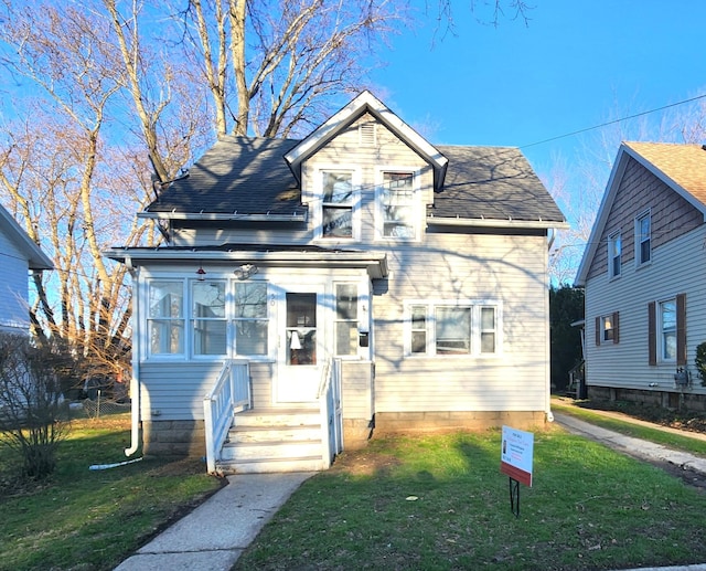 bungalow-style house with a shingled roof, a sunroom, and a front lawn