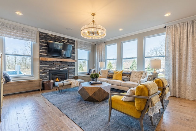living room featuring crown molding, light wood-style floors, a stone fireplace, recessed lighting, and a notable chandelier