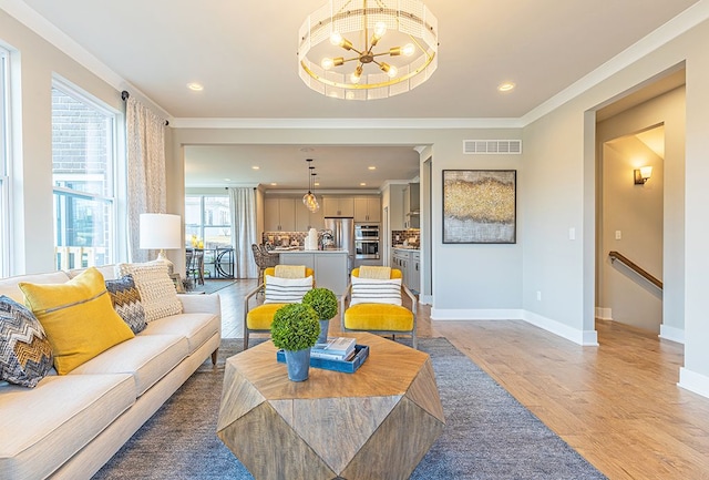living area featuring baseboards, an inviting chandelier, crown molding, visible vents, and light wood finished floors