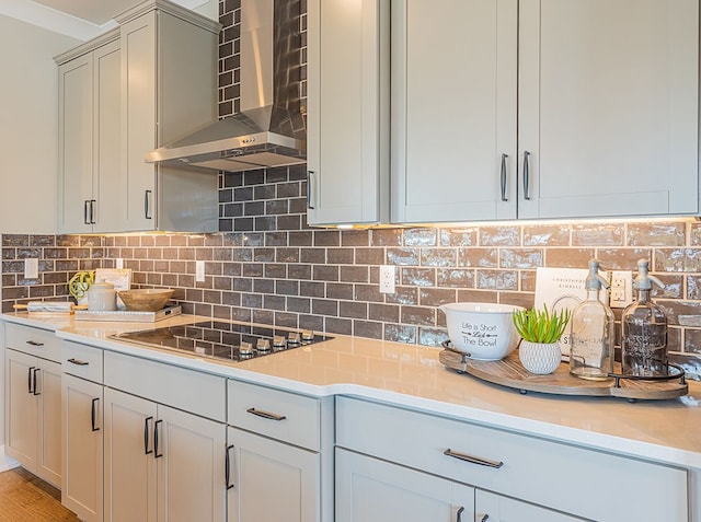 kitchen featuring light countertops, wall chimney exhaust hood, black electric stovetop, and decorative backsplash