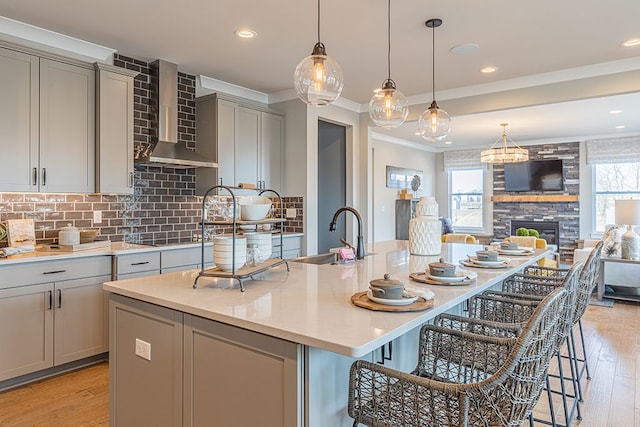 kitchen with a sink, wall chimney range hood, gray cabinetry, and crown molding