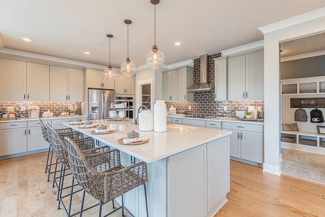 kitchen featuring ornamental molding, wall chimney range hood, appliances with stainless steel finishes, decorative backsplash, and a breakfast bar area