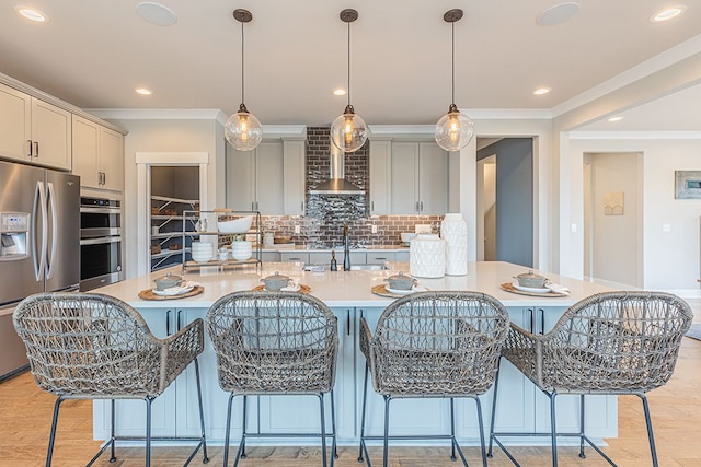 kitchen featuring crown molding, wall chimney exhaust hood, appliances with stainless steel finishes, light countertops, and backsplash