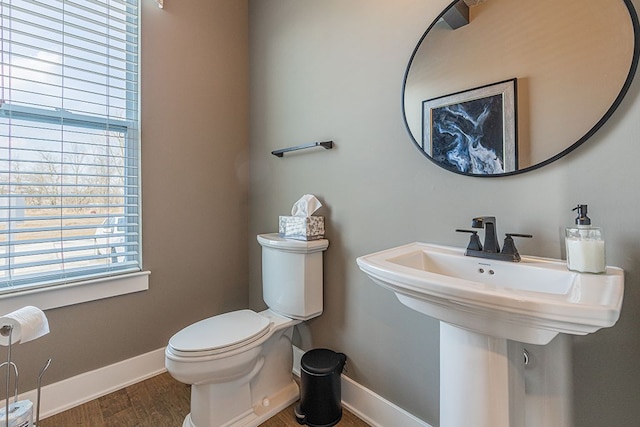 half bath featuring a sink, toilet, wood finished floors, and baseboards