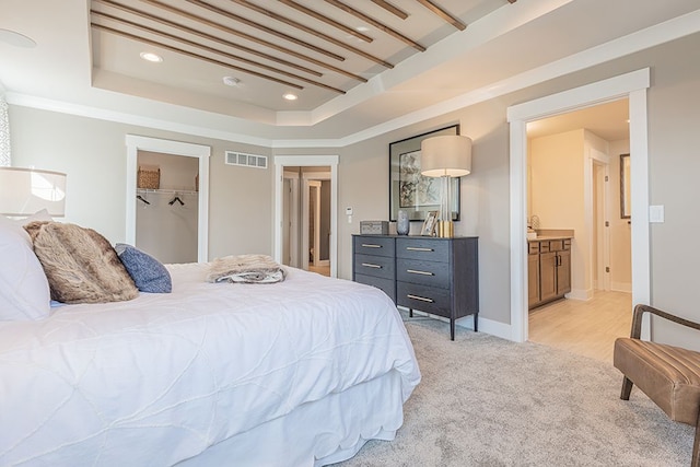 bedroom featuring ornamental molding, ensuite bathroom, visible vents, a raised ceiling, and light colored carpet
