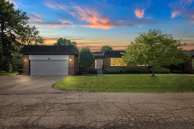 view of front of house featuring an attached garage, a yard, driveway, and brick siding