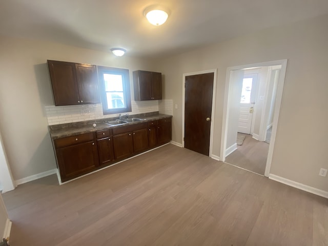 kitchen with light wood finished floors, a sink, tasteful backsplash, dark brown cabinets, and dark countertops