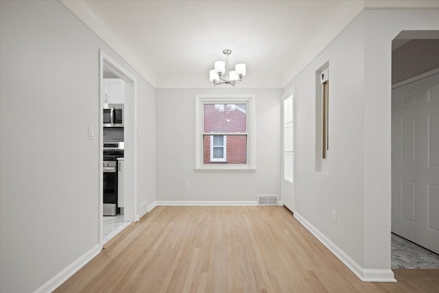 unfurnished dining area featuring light wood finished floors, a notable chandelier, baseboards, and visible vents