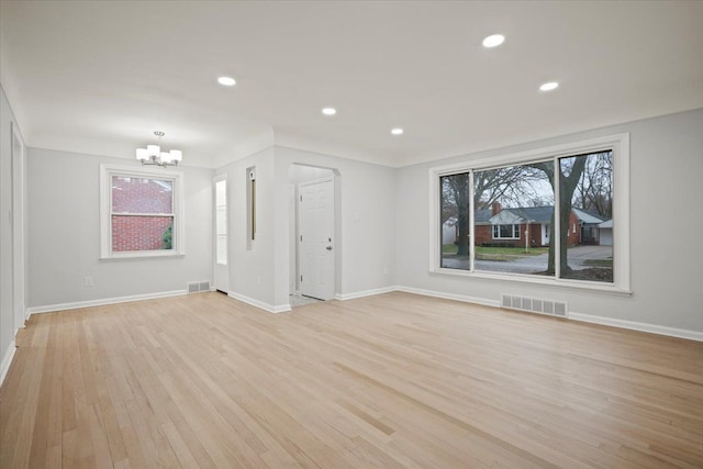 unfurnished living room featuring a chandelier, light wood finished floors, baseboards, and visible vents
